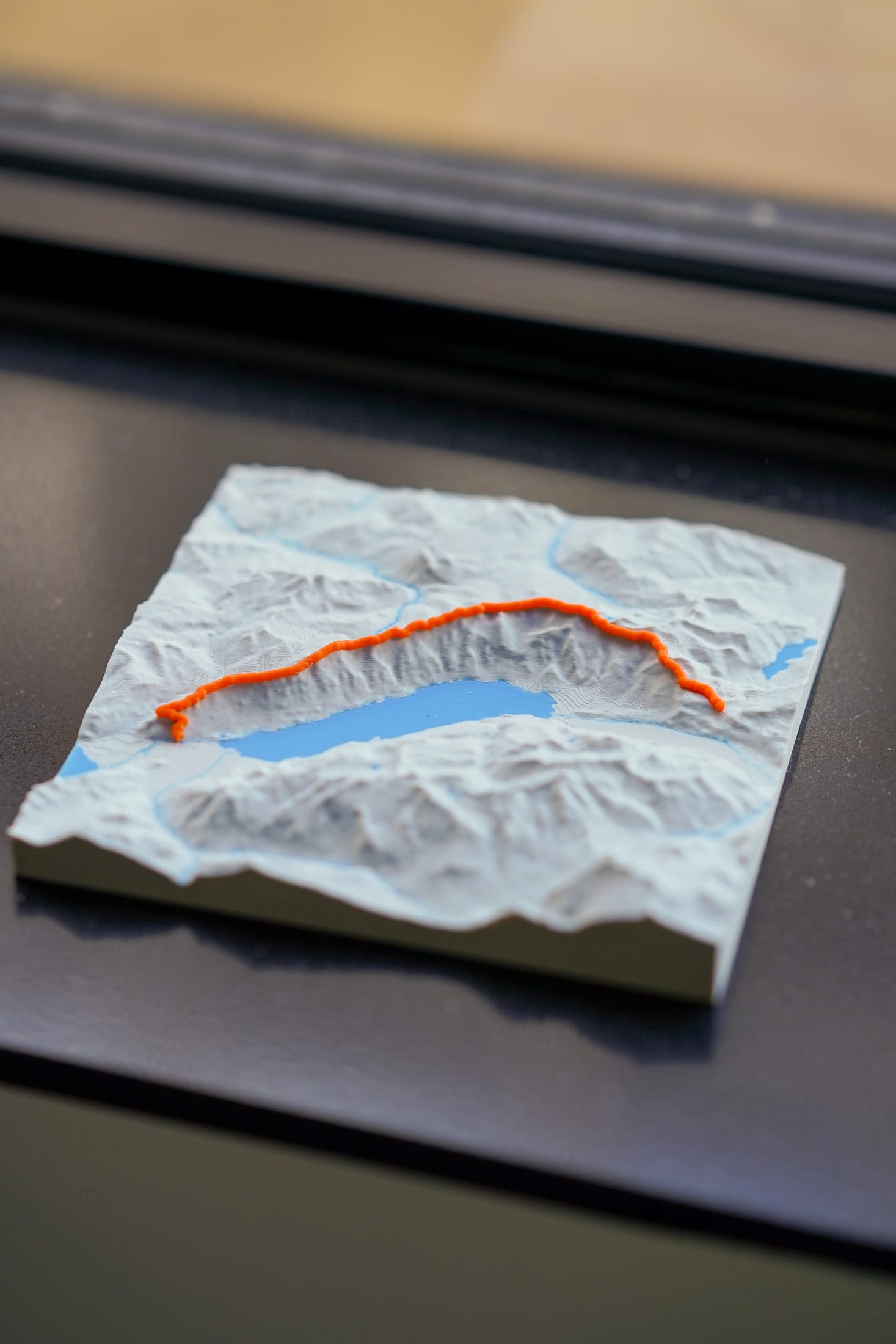 Close-up of an unframed minimal relief terrain tile with the orange route raised over the surface.